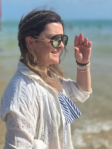 Cliente sorrindo de perfil na praia, usando os Óculos Tropea com armação tartaruga e hastes douradas.