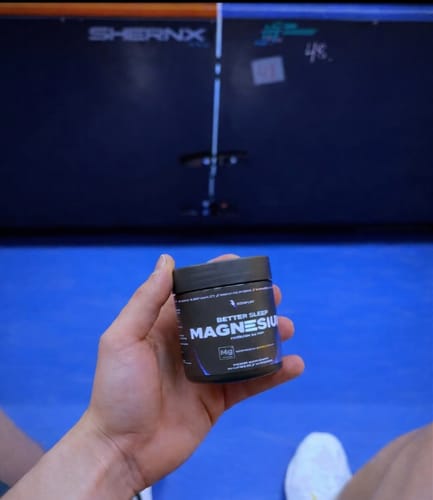 A customer holds up a small black jar of Sleep Magnesium in a gym.