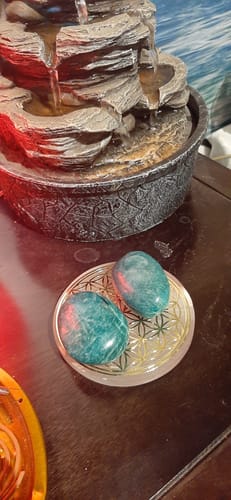 Deux galets Amazonite d'un client, polis et bleu-vert, sur une plaque de rechargement devant une fontaine.