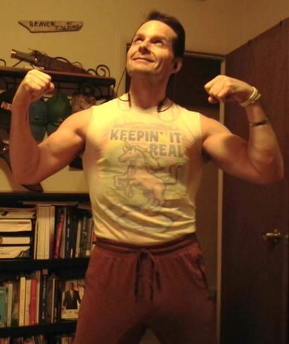 Reviewer in a yellow tank top, flexing and smiling while looking up in a room.