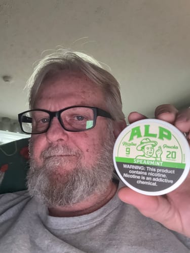 Reviewer holds up a white and green can of Spearmint Nicotine Pouches.