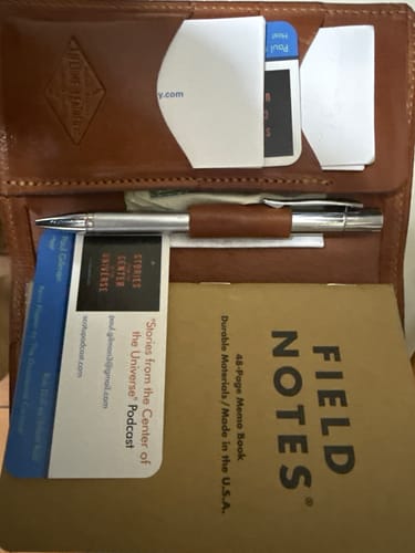 Customer's brown leather wallet cover shown open with a pen, Field Notes notebook, and cards neatly organized inside.