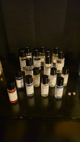 Customer's large collection of small fragrance bottles from the scent set on a dark surface.