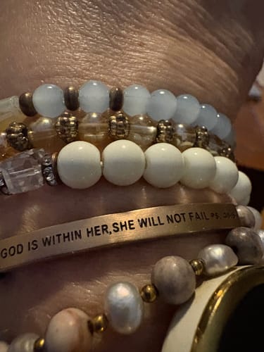 Close-up of a reviewer's wrist wearing the 'GOD IS WITHIN HER, SHE WILL NOT FAIL' bracelet stacked with other beaded bracelets.