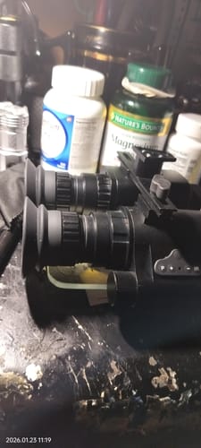 A reviewer's blurry image of miscellaneous items on a cluttered surface, including night-vision goggles and supplement bottles.