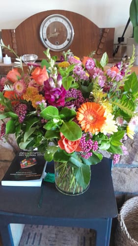 Customer's vibrant First Spring Blooms bouquet in a glass vase displayed on a side table.