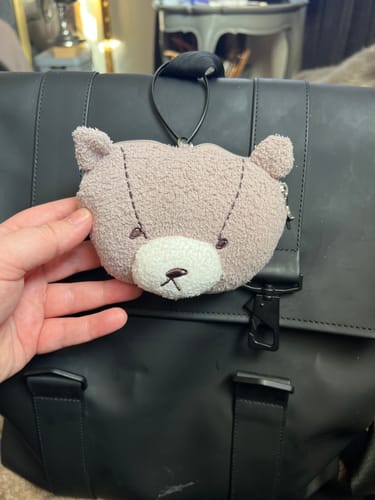 Customer holding the soft Jin's Bear Pouch Charm attached to the top of a black backpack.