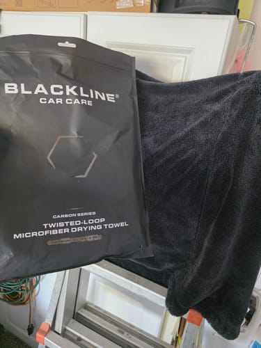 Customer's dark Twisted-Loop Drying Towel shown unfolded next to its black product packaging.