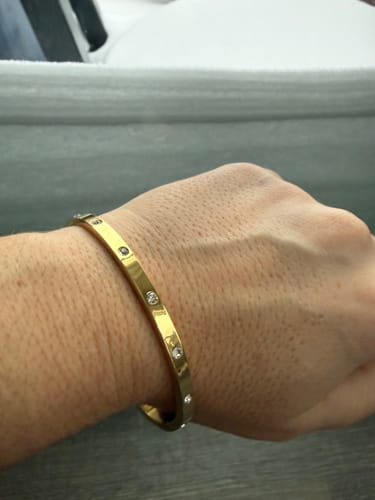 Close-up of a reviewer's wrist wearing the shiny gold Vina Bracelet with small inset stones.