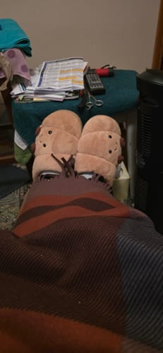 Customer relaxing with their feet up, wearing the cute Happy Croissant Slippers under a blanket.