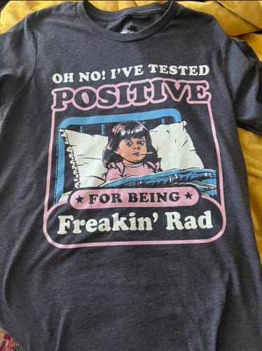Reviewer's dark grey graphic tee laid flat, showing the full 'I've Tested Positive For Being Freakin' Rad' retro design.