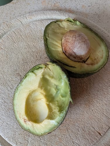 Ein Kunde zeigt eine aufgeschnittene, cremige Reed-Avocado auf einem Schneidebrett.