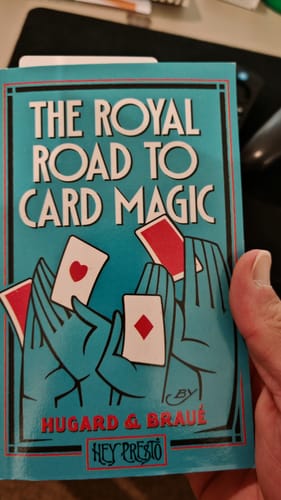 Customer holding the teal-covered book 'The Royal Road To Card Magic' by Hugard & Braue.
