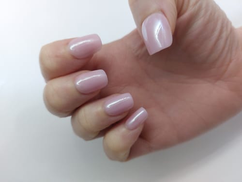 Customer's hand wearing the short, square Bridesmaid press-on nails with a shimmery pink finish.