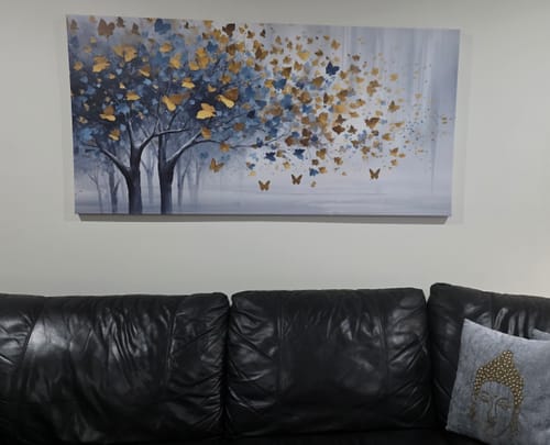 Customer's 'A Touch of Blue in a Golden Grove' canvas print displayed on a wall over a dark sofa.