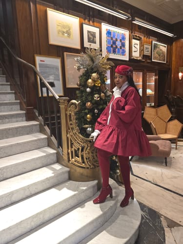 Reviewer posing on a staircase in the burgundy A-line mini dress with long puff sleeves and a white lapel.