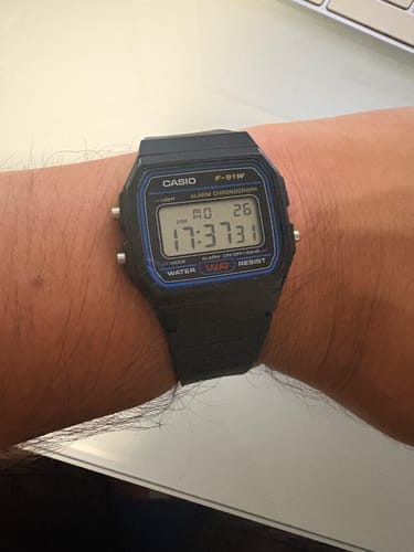 Cliente usando su reloj Casio F-91W negro con líneas azules en la muñeca.
