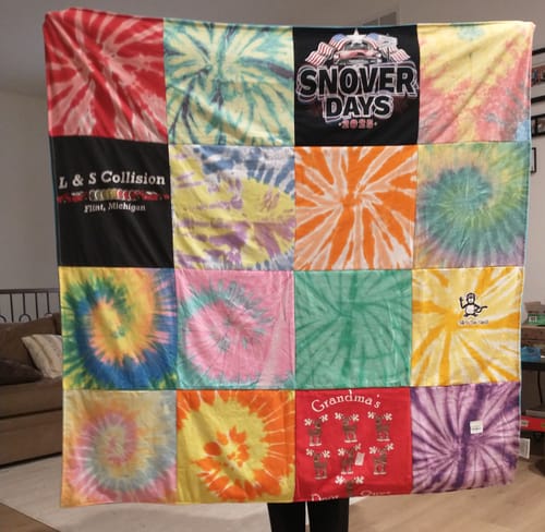 Reviewer holding up their custom Premium T Shirt Quilt, made from many colorful tie-dye shirts.