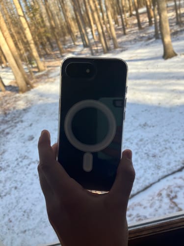 Customer's hand holds a dark phone in the MagCase Clear, showing the white magnetic ring against a snowy background.