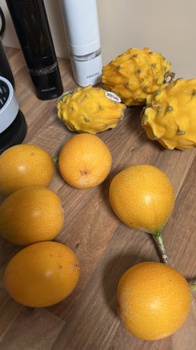 Ein Kunde zeigt mehrere frische, süße Granadillas auf einer Holzoberfläche.