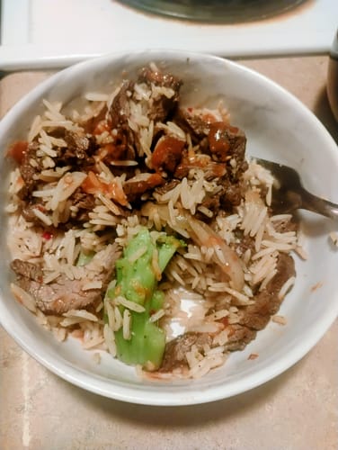 Reviewer's bowl of Mongolian Beef showing rice, beef, and a broccoli stem with added red sauce.