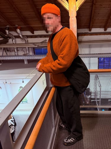 Reviewer wearing the black Wide-Strap TØTE Bag crossbody while standing on an indoor balcony.