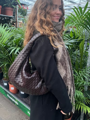 Reviewer carrying the dark brown woven bag over their shoulder while in a plant shop.