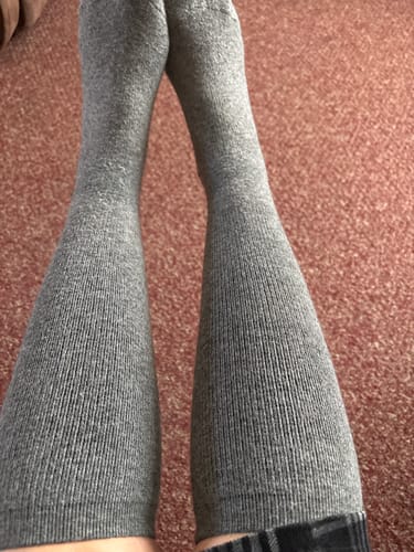 Customer's legs crossed at the ankles, wearing long grey Alpaca Socks.