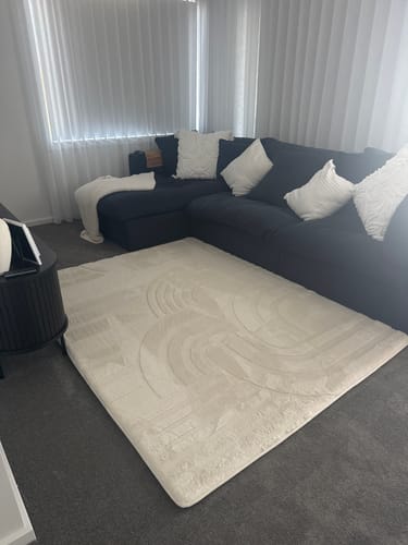 Customer's soft Vanilla Cream Mellow Mat with a carved design, placed in a modern living room next to a dark sofa.