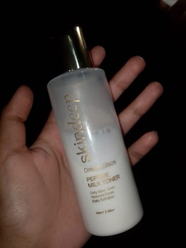 Reviewer holds the DREAM GLAZE Peptide Milk Toner in their hand, showing the milky liquid inside the bottle.