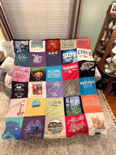Customer's colorful Premium T Shirt Quilt made from many different t-shirts, draped over the back of a sofa in a living room.