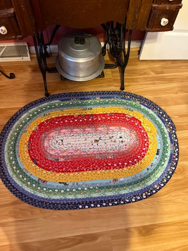 Reviewer's colorful, oval jelly-roll rug made from the Ambassador Box, shown on a wood floor.