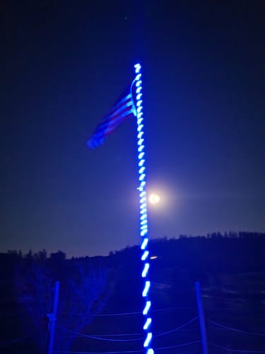Customer's Ultra Heavy Duty American Flag on a blue-lit flagpole at night, with the moon visible in the sky.