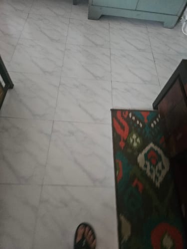 Partial view of a customer wearing the black Frido Cloud Comfort Slipper on a tiled floor.