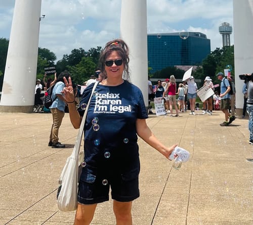 Customer wearing the blue "Relax Karen I'm Legal" t-shirt while making a peace sign at an outdoor march.