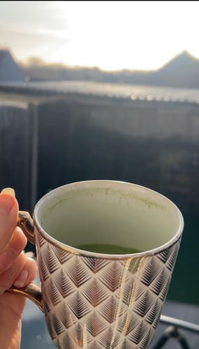 Close-up of a reviewer's hand holding a decorative mug filled with green DIRTEA Matcha.