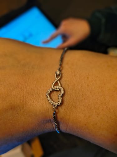 Customer wearing the Forever Love Bracelet, showing its crystal-paved heart and infinity symbol on their wrist.