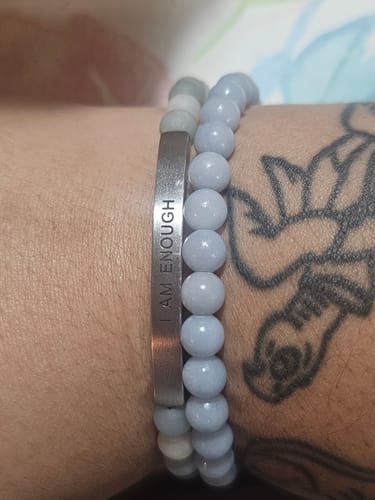 Customer's wrist wearing the engraved 'I AM ENOUGH' bracelet next to a light blue beaded bracelet.