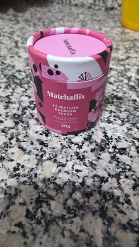 Cliente mostrando el envase rosa del Té matcha del mes, sabor fresa, sobre una encimera.