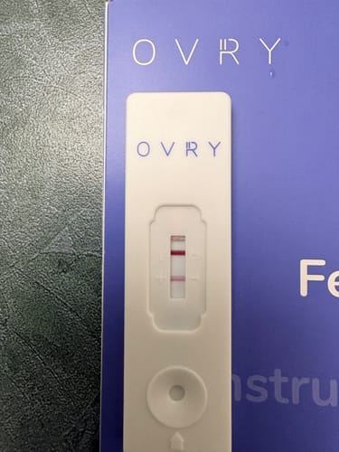 Customer's Ovry Male Fertility Test cassette showing a result with two red lines in the test window, placed on its packaging.