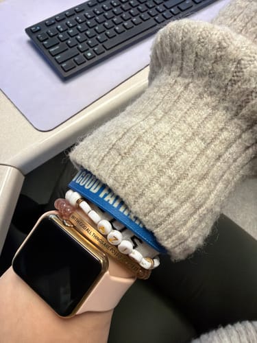 Customer's wrist showing the 'WITH GOD ALL THINGS ARE POSSIBLE' bracelet stacked with other bracelets and a watch at a desk.