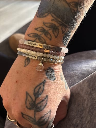 Customer's tattooed wrist with a stack of bracelets, including the Pink Quartz accent and an engraved 'You are my sunshine' bar.