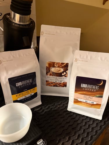 Reviewer's bag of Neapolitan Dark Roast Espresso Blend on a counter with other coffee blends and an espresso grinder.