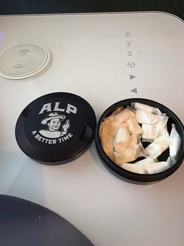 Customer's open black tin of Spearmint Nicotine Pouches, with the lid next to it showing the white pouches inside.