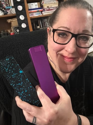 Reviewer holding a purple pill case and a black pill case with a blue splatter design.