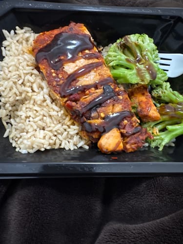 Customer's Fit Salmon meal in a black container, showing the salmon with a dark sauce, brown rice, and broccoli.