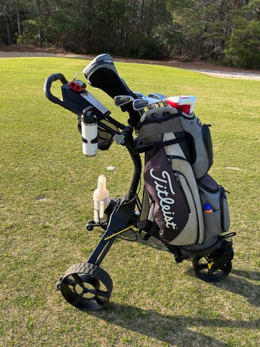 Customer's black Cybercart holding a golf bag and accessories on a sunny golf course.