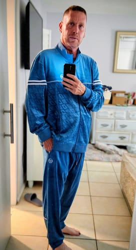 Customer taking a mirror selfie while wearing a blue velour tracksuit in a room.