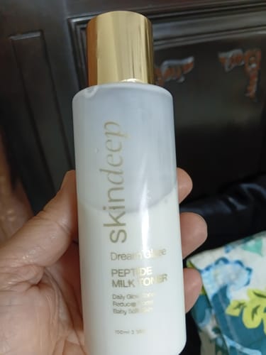 Reviewer holding the DREAM GLAZE Peptide Milk Toner in its white bottle with a gold cap.