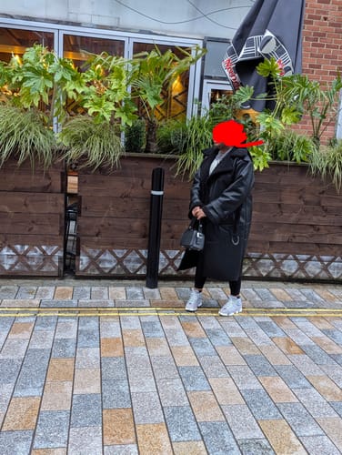Reviewer standing outdoors wearing the long, black Cora Faux Leather Maxi Coat with leggings and sneakers.